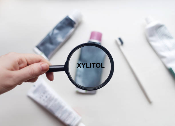 xylit in natürlicher zahnpasta. die lupe ist auf ein röhrchen gerichtet, in dem sich die inhaltsstoffe eines sicheren produkts befinden. sichere zahnpasta-zusammensetzung - emaille-auf-platte stock-fotos und bilder