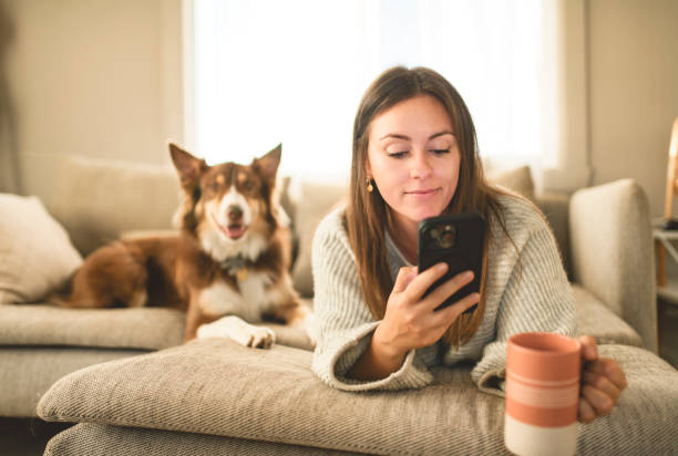 istock woman drinking coffee and using cellphone on the morning with cute fluffy Australian Shepherd dog at home in living room 2185565523