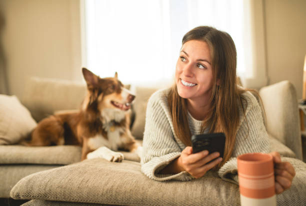 istock woman drinking coffee and using cellphone on the morning with cute fluffy Australian Shepherd dog at home in living room 2185565527