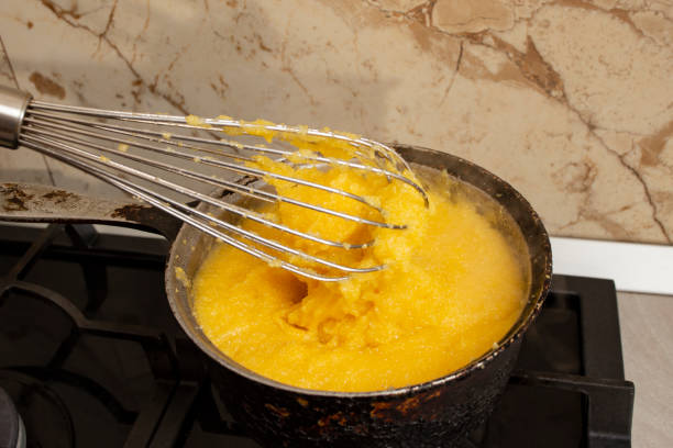 Boiling corn flour in a cast iron pot, making mamaliga, traditional romanian food, and mixing with a stainless steel whisk, soft focus close up Boiling corn flour in a cast iron pot, making mamaliga, traditional romanian food, and mixing with a stainless steel whisk mamaliga stock pictures, royalty-free photos & images