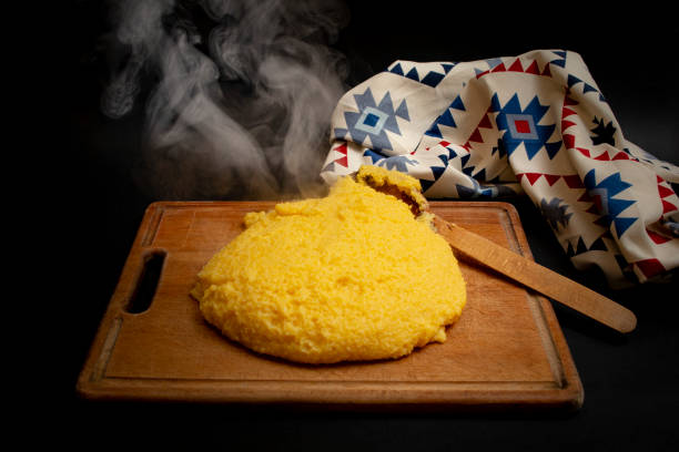 Romanian traditional mamaliga on a wooden chopping board next to a eastern motifs table cloth, on dark background Romanian traditional mamaliga on a wooden chopping board next to a eastern motifs table cloth mamaliga stock pictures, royalty-free photos & images