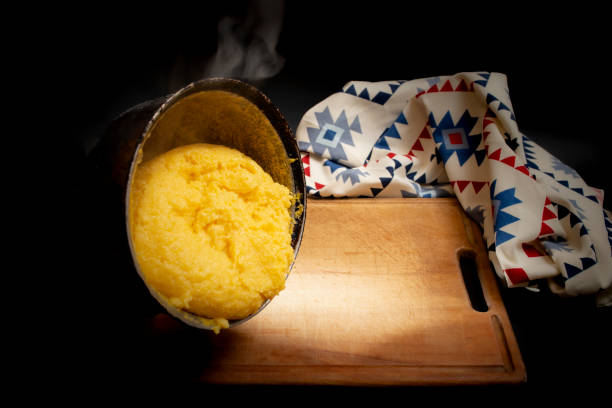 Romanian traditional mamaliga pouring on a wooden chopping board next to a eastern motifs table cloth, on dark background Romanian traditional mamaliga on a wooden chopping board next to a eastern motifs table cloth, mamaliga stock pictures, royalty-free photos & images