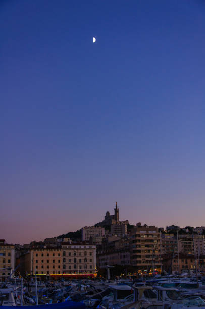 High Moon in the night sky over the evening Marseille, France. Castle tower on a hill above the city.