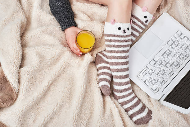 istock Woman on bed with bear socks and orange juice using a laptop 2185571915