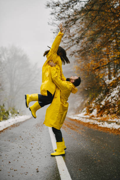 istock Boyfriend Holding Girlfriend Above Head While Both Are Wearing Waterproof Clothes Standing on Road 2185573255