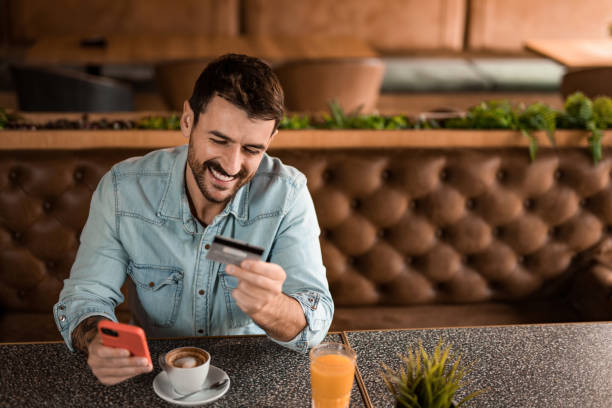 istock Cheerful man using online banking in coffee shop. 2185577454