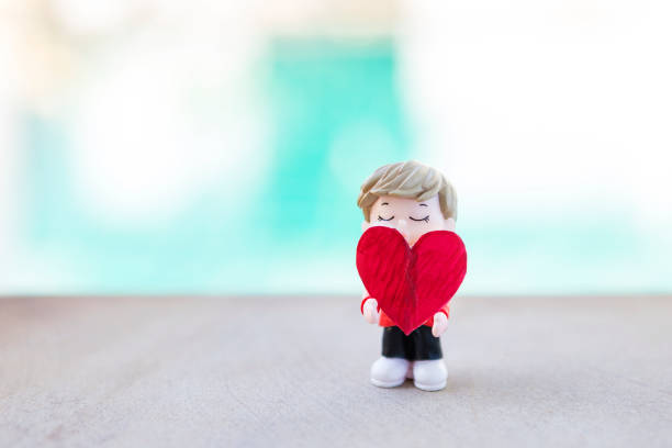 Miniature boy holding red heart with space on blurred background, outdoor day light, valentine concept background idea