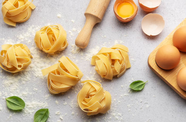 Fettuccine pasta nests with basil, eggs, flour and rolling pin on kitchen table