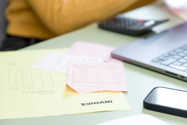 Focused accountant working on invoices with laptop and calculator in cluttered office, ensuring accurate billing and budgeting in small business setting