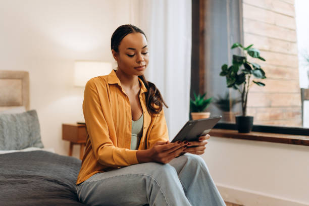 istock Positive African American woman using digital tablet while resting on bed at home 2185587544