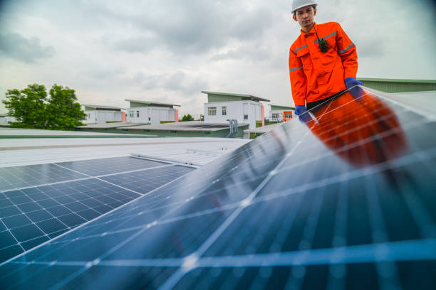 istock A worker in an orange safety jacket inspects solar panels on a rooftop, using a laptop to ensure proper maintenance. The scene highlights renewable energy, solar technology, and sustainable practices. 2185595439