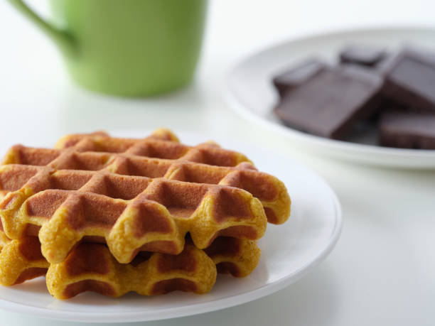 Plates of homemade gluten free waffles and broken dark chocolate on a table near a mug.