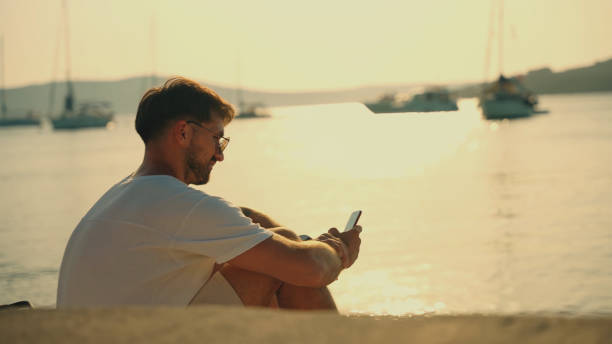istock Man Texting on Mobile Phone by the Sea with Yachts in Background 2185597605