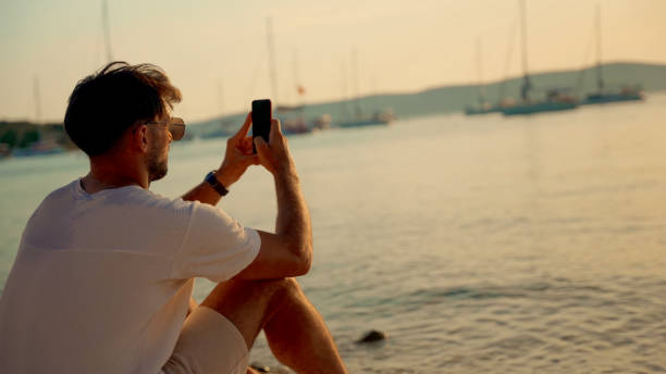 istock Man Taking Photos on Beach with Yachts in Background 2185597606