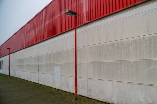 Red metal siding contrasts with a white concrete wall along a desolate industrial building, a solitary lamppost standing guard
