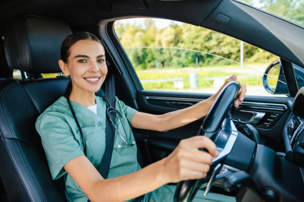 istock Smiling beaming young woman in scrub suit driving a car 2185601087