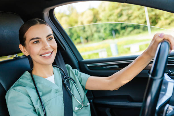 istock Smiling beaming young woman in scrub suit driving a car 2185601090