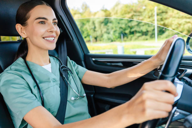 istock Smiling beaming young woman in scrub suit driving a car 2185601100