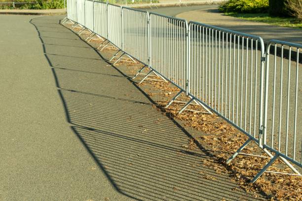 Long metal crowd control barriers casting shadows on asphalt road