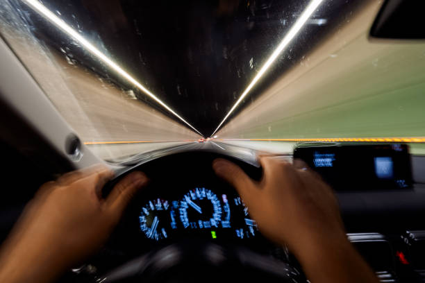 Driver races through a dim tunnel at night, gripping the wheel with blurred motion, embodying urgency and freedom. The view captures adventure and independence as lights illuminate the road ahead