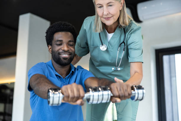 istock Young male patient exercising with dumbbells with a physical therapist 2185603991