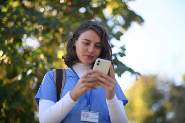 Beautiful nurse in uniform holding smartphone in hands, scrolling, looking at device screen.