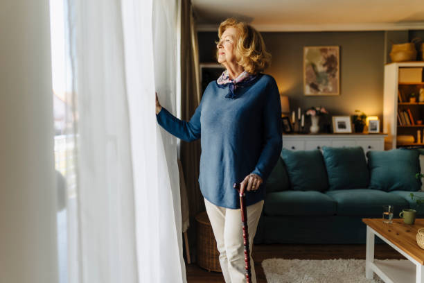 istock Senior woman standing by a window with a cane 2185607351