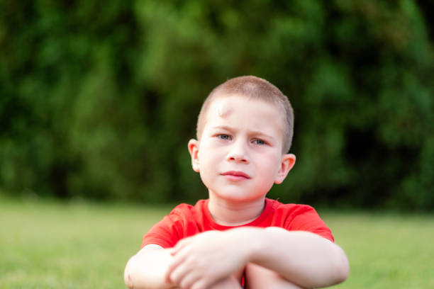 boy sitting on the meadow unhappy looking at the camera has a rainbow