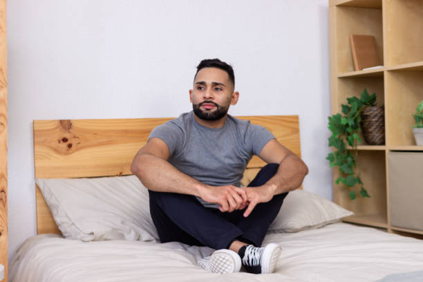 istock Young man sitting thoughtfully on bed in modern bedroom 2185609407