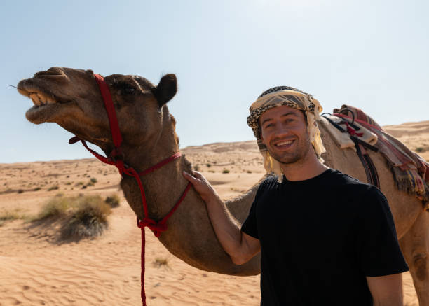 istock Man Standing Next to a Camel in Wahiba Sands, Oman 2185612107