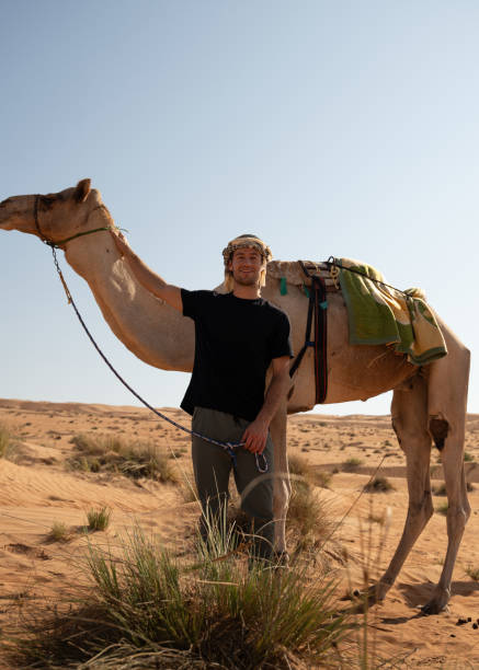 istock Man Standing Next to a Camel in Wahiba Sands, Oman 2185612259