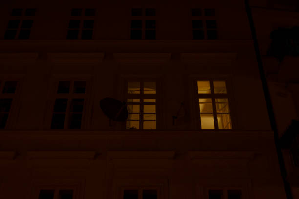 In a cozy apartment, a dimly lit window contrasts with the night outside, revealing a solitary satellite dish and reflecting urban life below, all under a tranquil, starry sky inviting introspection