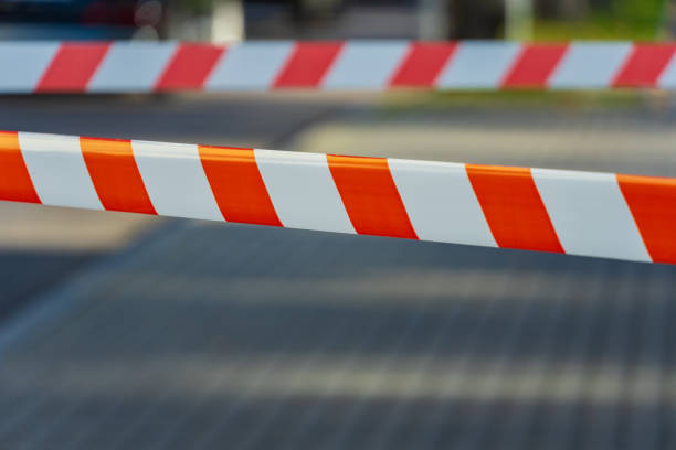 istock Caution tape stretches across a pathway, creating a vibrant barrier that signals restricted access. Sunlight shines brightly, illuminating the bold orange and white stripes, enhancing visibility 2185617620