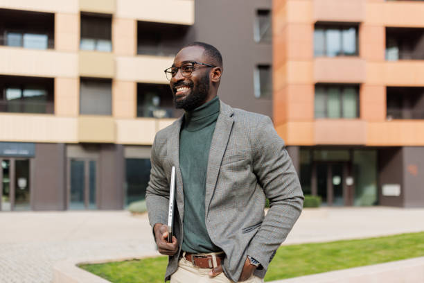 istock Man in gray blazer holding laptop outside urban building complex. 2185618757