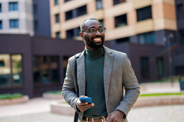 istock Smiling man with smartphone in urban setting, modern attire. 2185618825