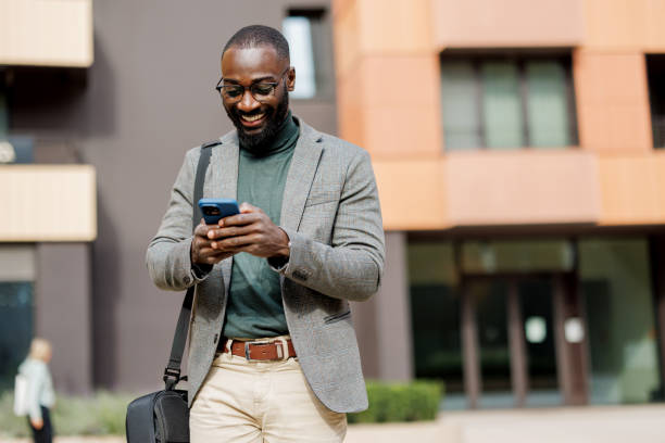 istock Man engaged with phone, smiling casually, urban architecture. 2185618834