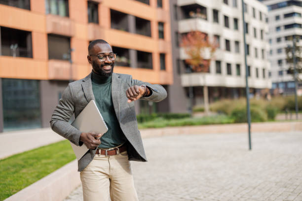 istock Man checks smartwatch while holding laptop outside modern building 2185618869