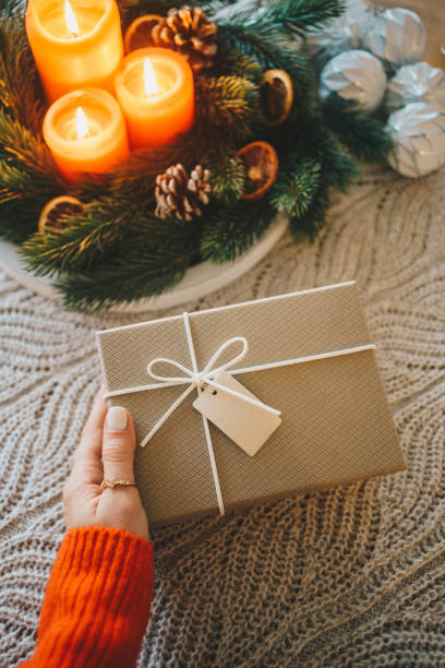 istock Woman hand holding gift box next to Christmas decorations on the table 2185620838