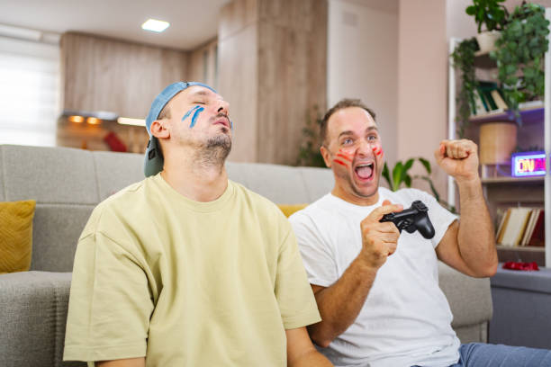 istock Two friends playing video games at home, one winning and one losing 2185628065