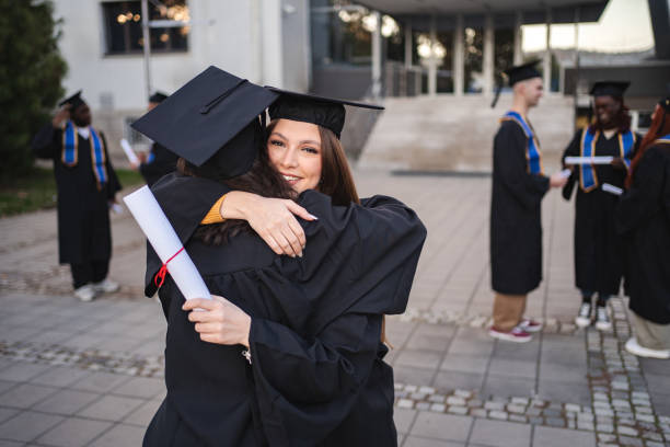istock Two happy young adults students are hugging each other after graduation ceremony 2185628406