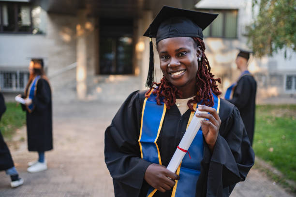 istock Young smiling graduate holding diploma posing at graduation ceremony 2185628408