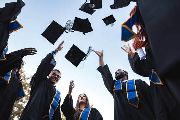 istock Happy students throwing graduation caps in the air 2185628417