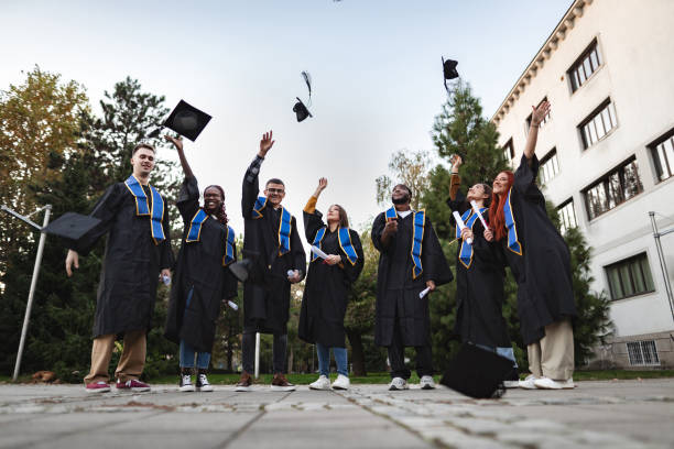 istock Happy graduates throwing graduation caps in the air 2185628473