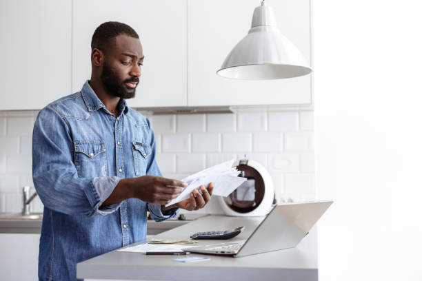 istock Man managing finances with a laptop and papers in a modern kitchen 2185632398