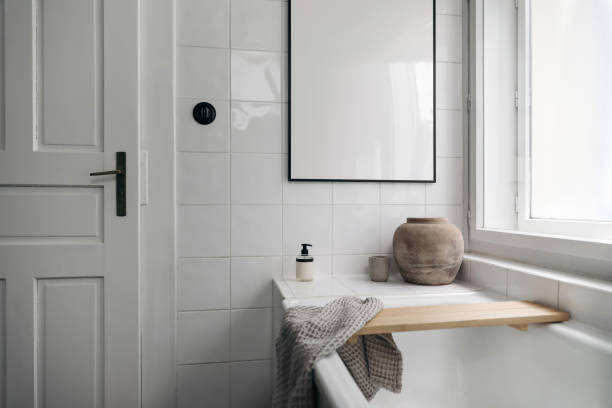 istock Stylish bathroom. Modern Scandinavian bathroom interior with bathtub. Black picture frame mockup. Framed poster on white tiles. Candle, towel and old vase. Blurred foreground. Ceramic switch. 2185637035