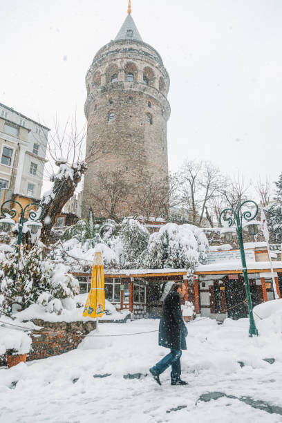 Istanbul, Turkey - January 8, 2017:  The historic Galata Tower stands tall amidst a serene snowy landscape in Istanbul. Covered in a soft blanket of snow, the surrounding area is alive with people walking through the frosty streets. The iconic tower, a symbol of the city’s rich history, provides a picturesque scene against the winter sky. The peaceful ambiance and the muted colors of winter make this a memorable moment in the heart of Beyoğlu.