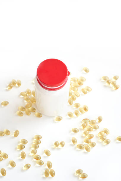 istock White bottle with red cap surrounded by scattered gold capsules on clean white 2185646403