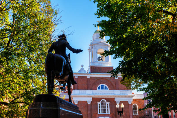Cambridge, MA, USA - June 29, 2022: A visitor to the Harvard Yard, the oldest part of the Harvard University campus in Cambridge, Massachusetts, touches the foot of the John Harvard statue.