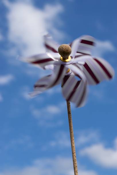 A colorful pinwheel spinning under a bright blue sky with scattered clouds.