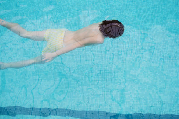 Joyful child swimming underwater in a bright blue pool on a sunny summer day, surrounded by clear turquoise water and mosaic tile patterns